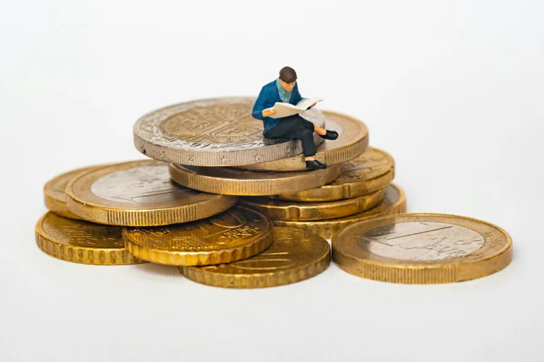 Miniature figure reading a newspaper while sitting on a pile of coins